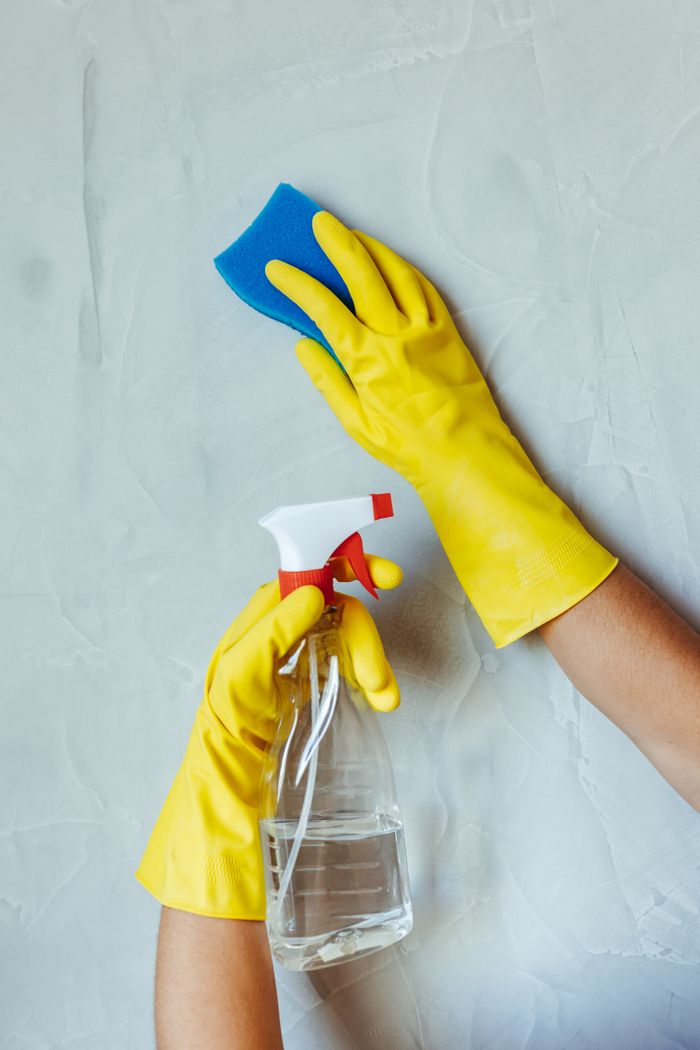 services-03 Hands in yellow gloves cleaning wall with sponge and spray bottle.